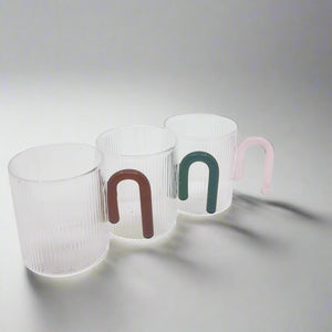 product photo of three clear glass mugs, each with a different colour handle