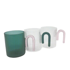 Product photo of 3 glass mugs sitting in a row. The first teal with a pink handle, then clear with a teal handle and clear with a pink handle