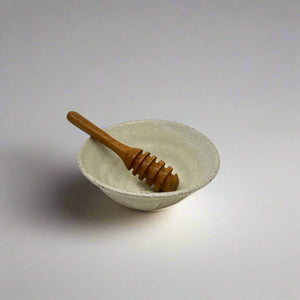 Product photo for a wooden honey dipper utensil. Dipper is sitting in small ceramic bowl