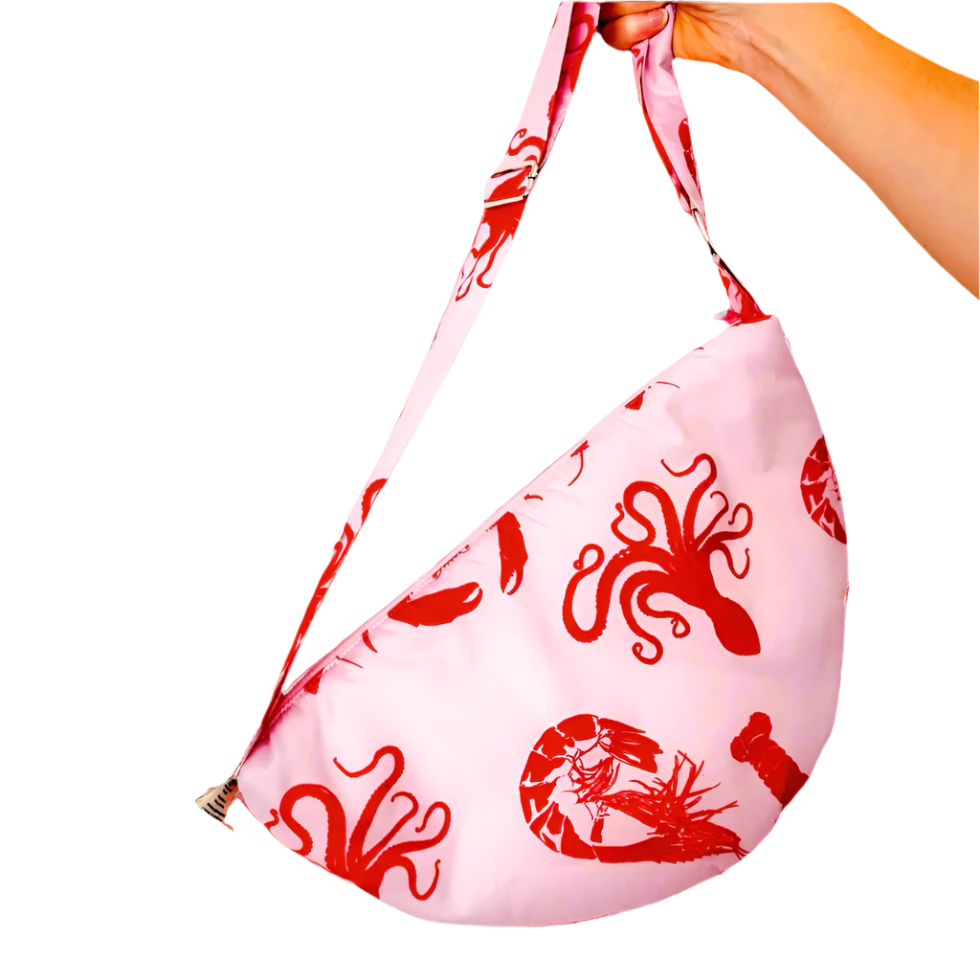product photo of fabric sling style bag. Pastel pink bag with red octopus and shrimp patterns. Hand is holding bag by the long strap