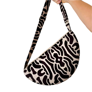 Product photo of fabric sling style bag, in abstract black and beige print. Hand is holding up bag by a long strap