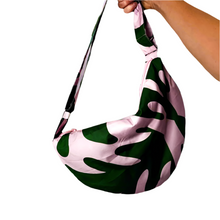 Cargar imagen en el visor de la galería, Product photo of fabric sling style bag, in dark green and pastel pink/lilac print. Hand is holding up bag by a long strap
