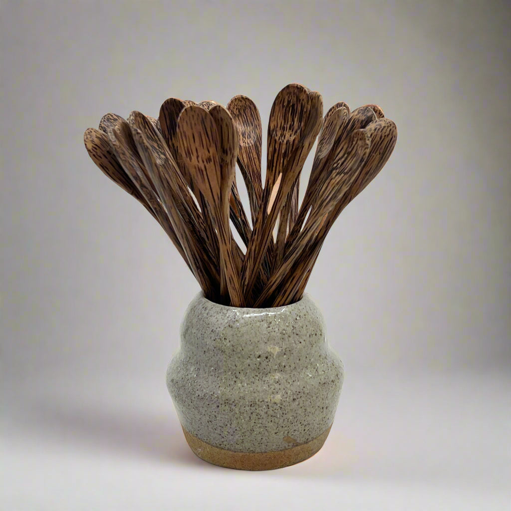 Product photo of hand carved long dark wood spoons. Multipal spoons sitting in a ceramic vase