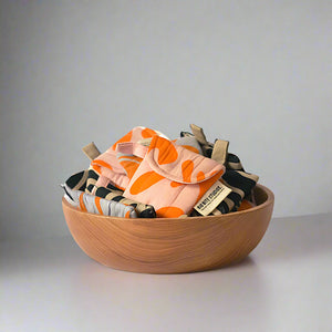 product photo for fabric airpod pouches. multiple colourful pouches sitting in a wooden bowl