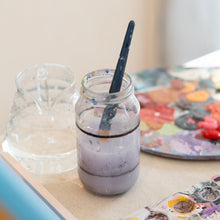 Load image into Gallery viewer, Mason jar with water and a paintbrush on a table with art supplies
