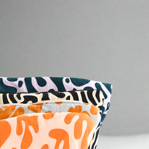 Product photo of a fabric sling bag, close up of corners, four bags shown in different bright abstract colours